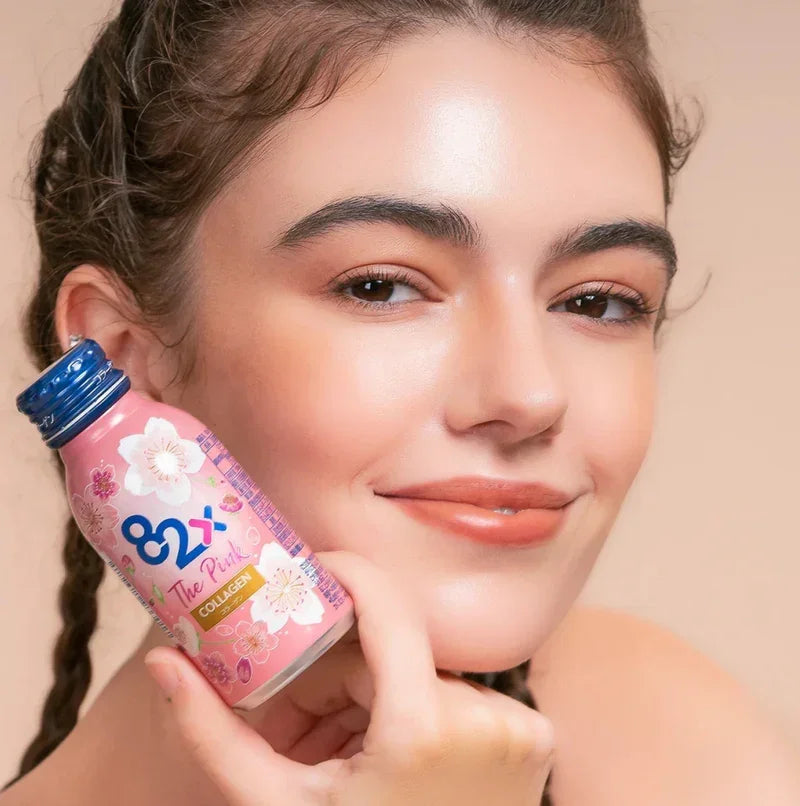 Smiling woman holding 82X The Pink Collagen supplement bottle for beauty and wellness.